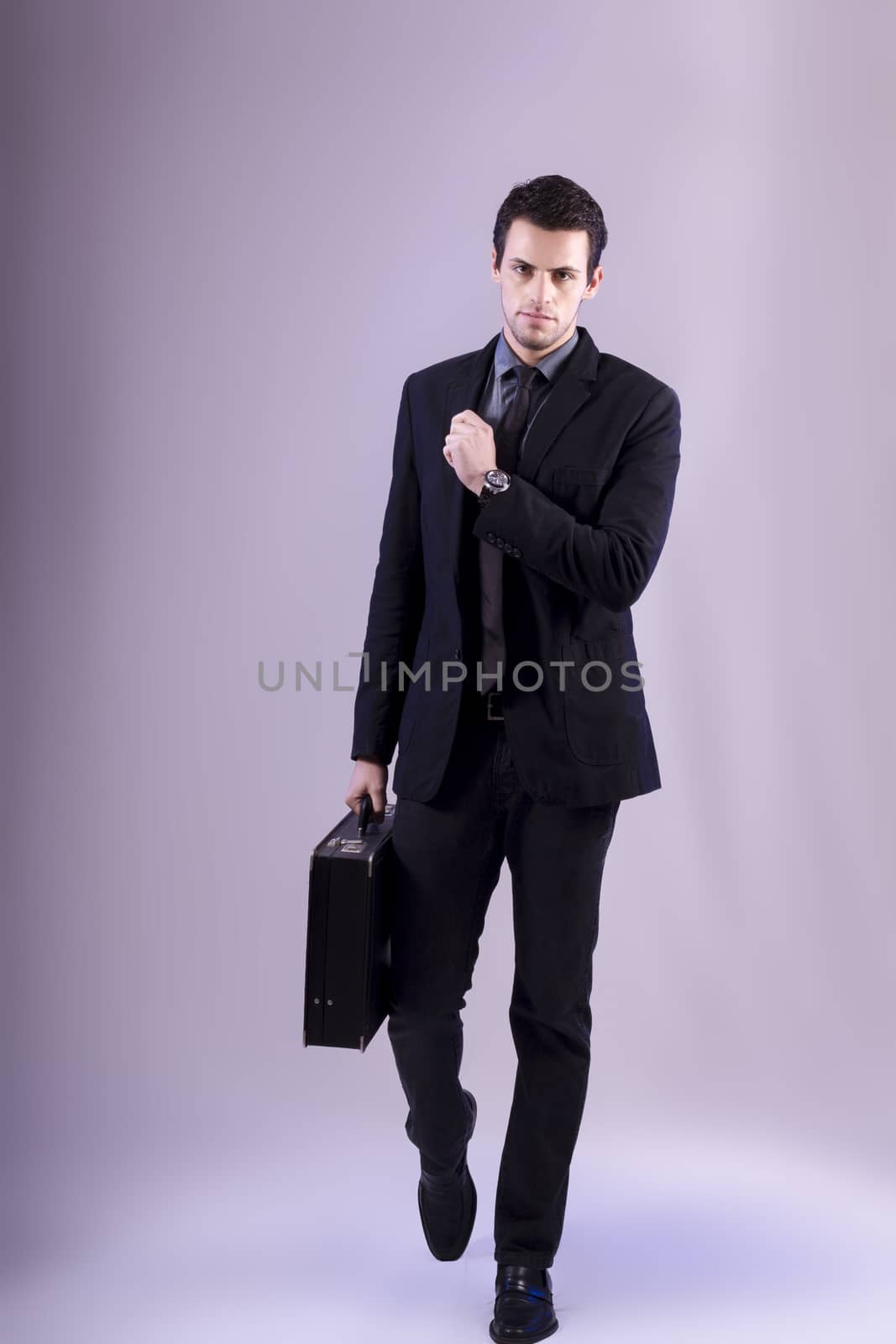 View of a young business man walking against a grey  background. 