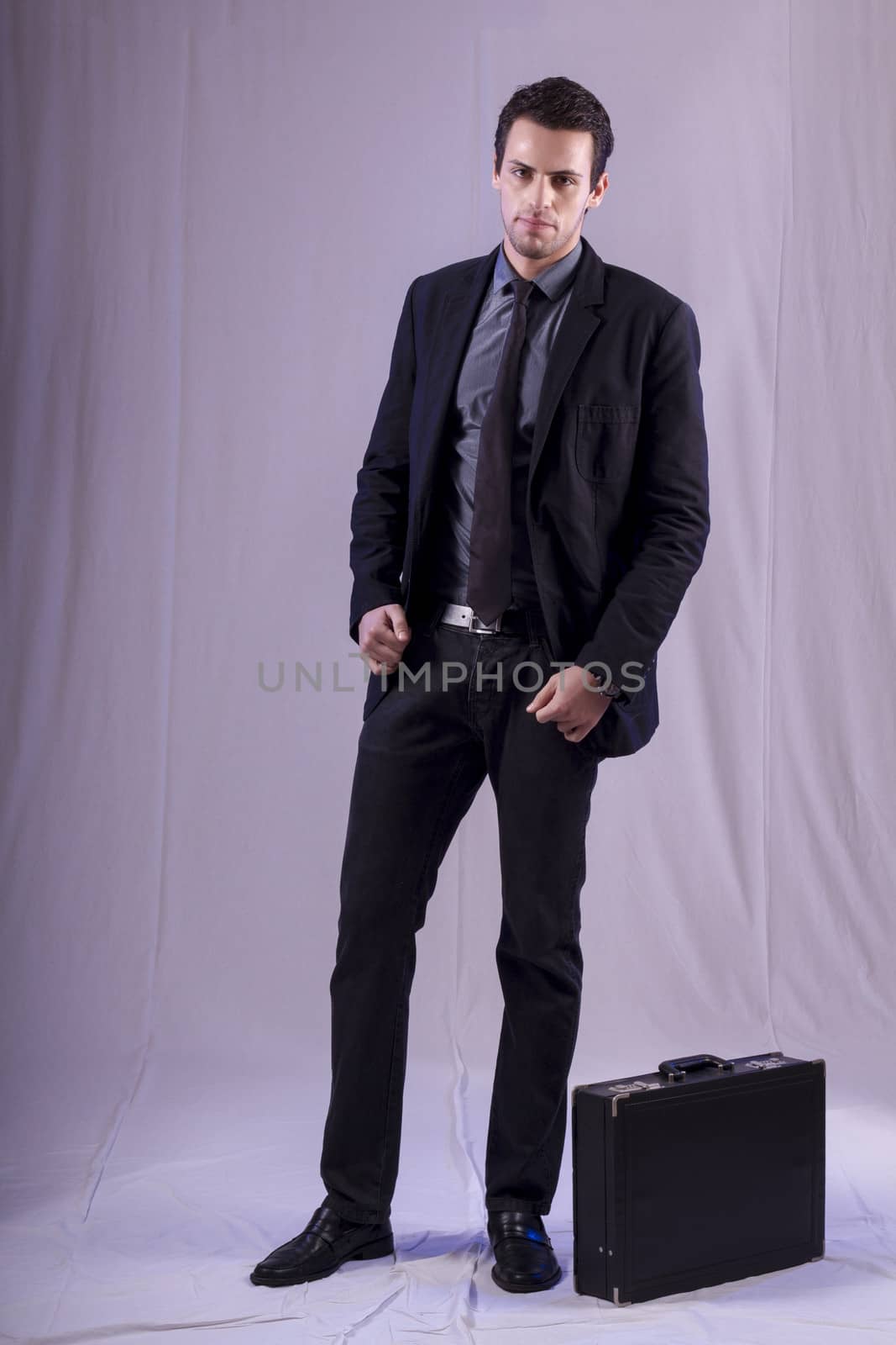 View of a young business man standing against a grey  background. 