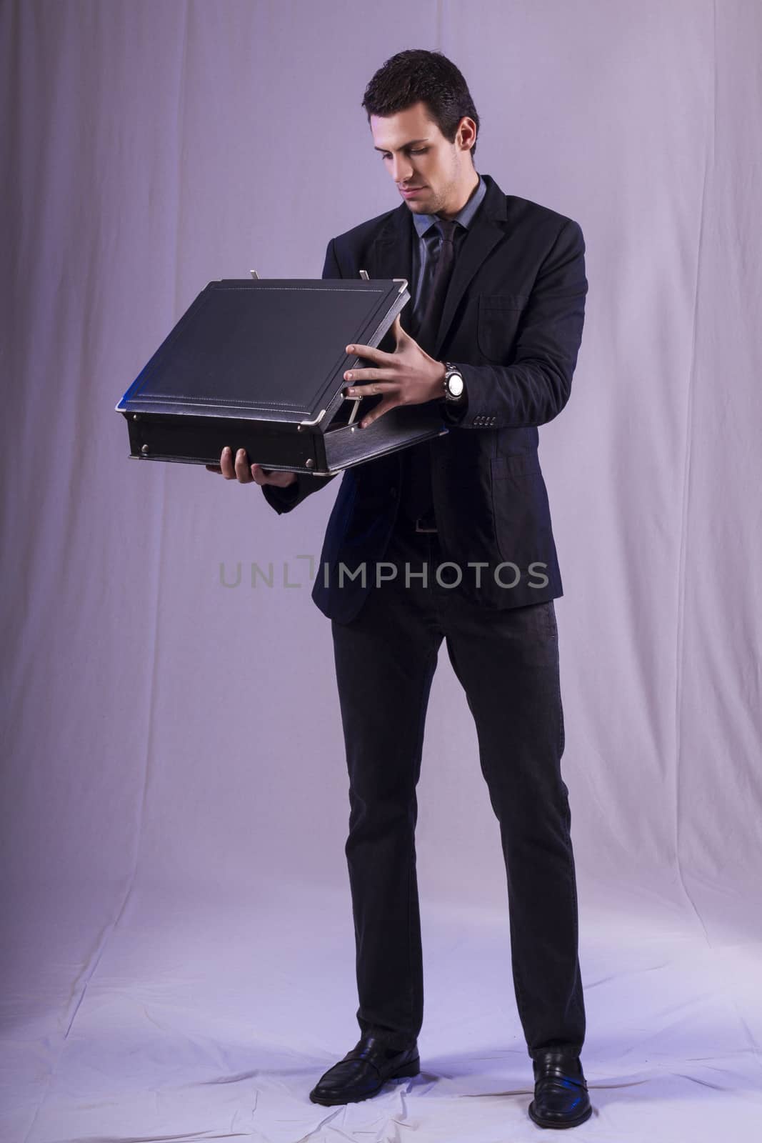 View of a young business man standing against a grey  background. 