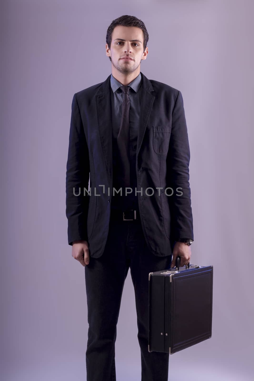 View of a young business man standing against a grey  background. 