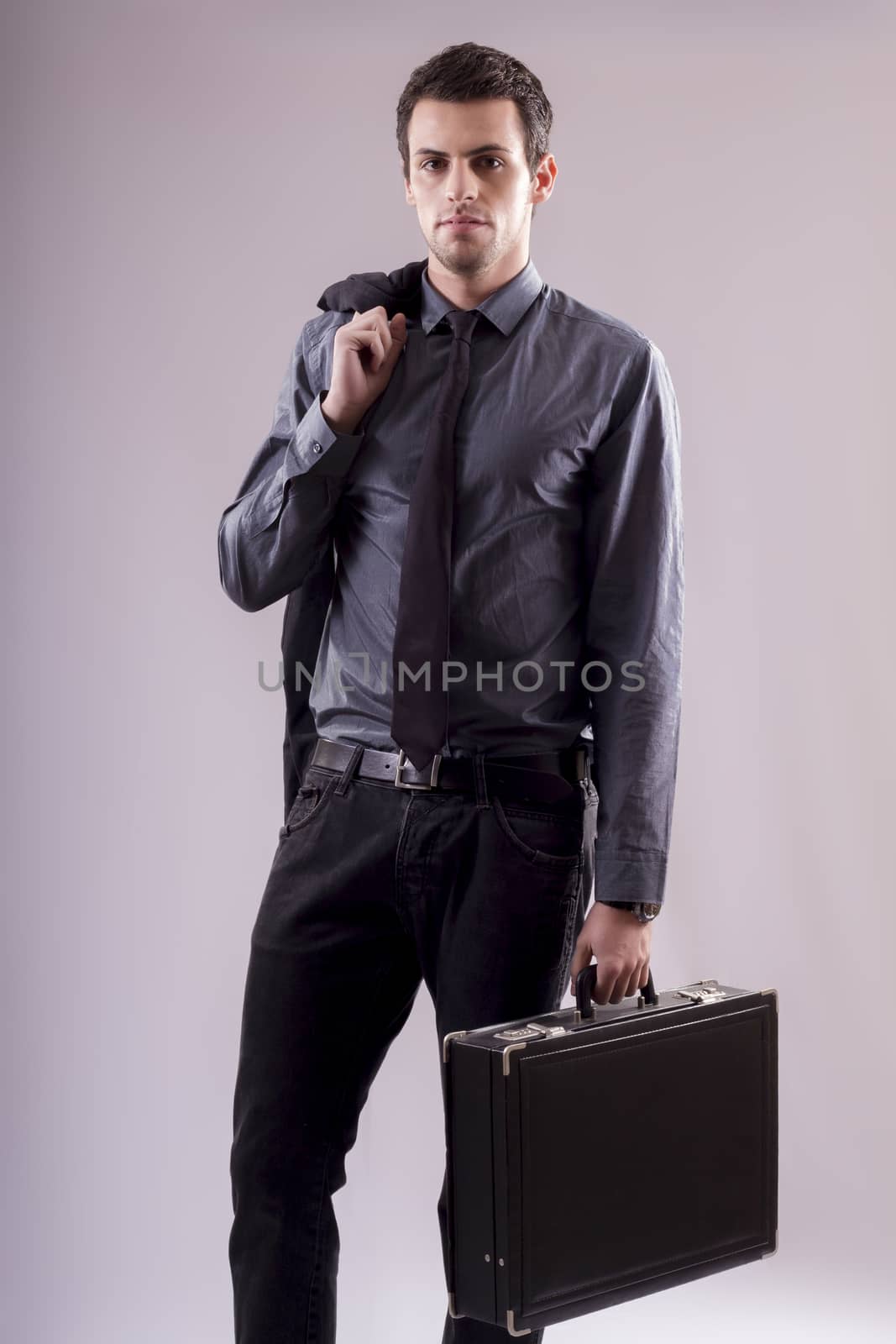 View of a young business man standing against a grey  background. 