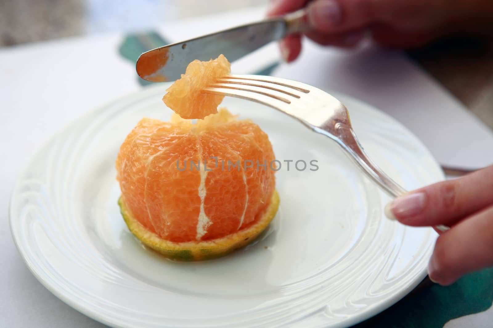close up of hands cuting slice of an orange with knife and fork on a white plate