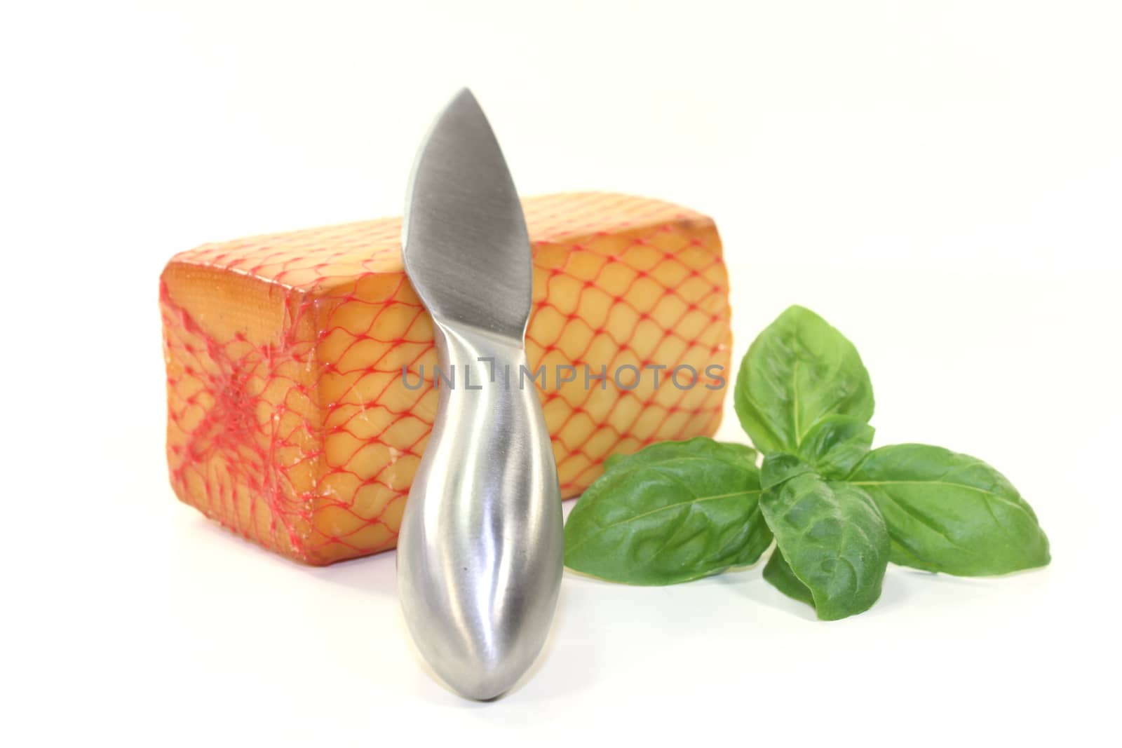 a piece of cheese with a cheese knife and basil