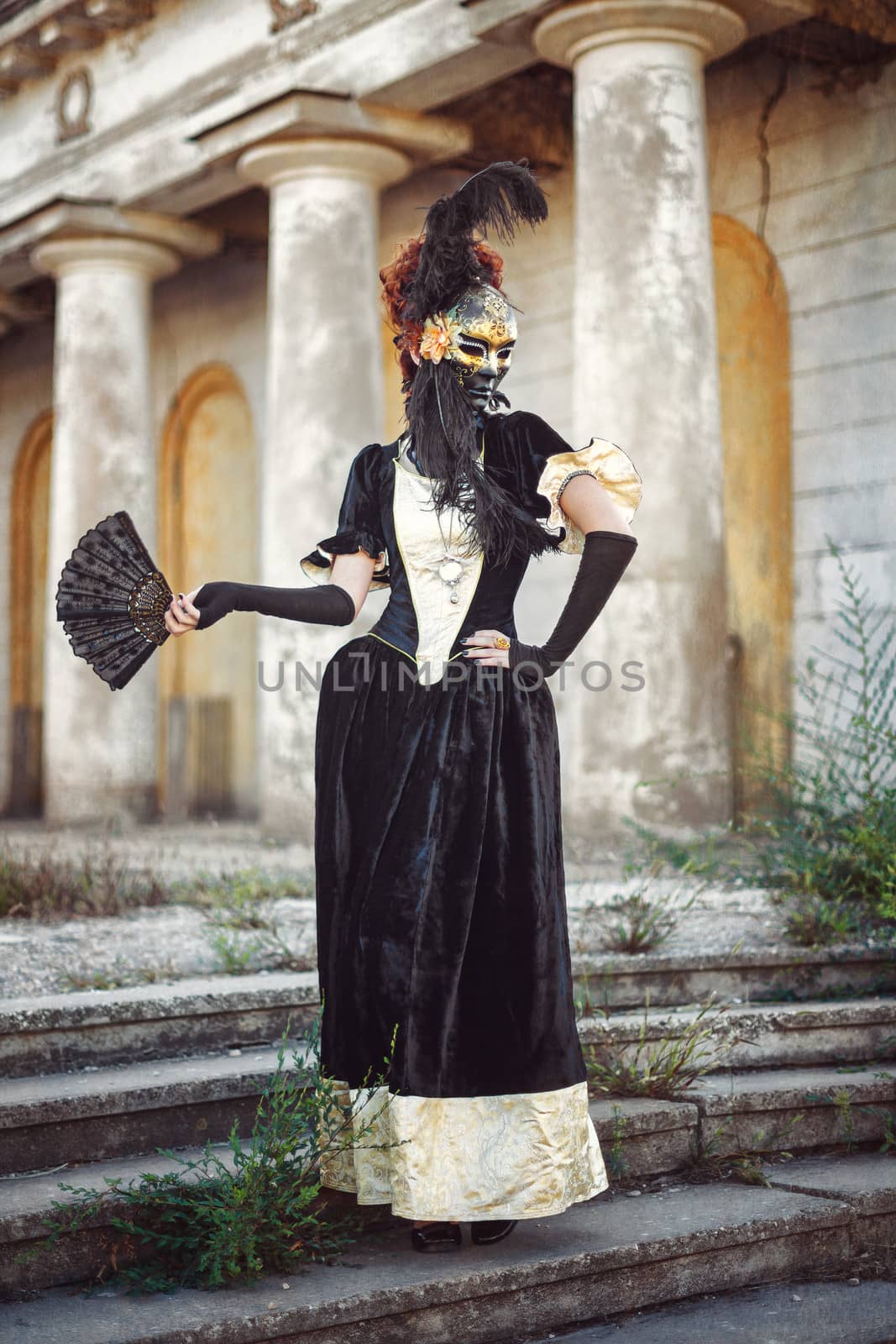 Portrait of red-haired woman holding a mask shot against the background of columns