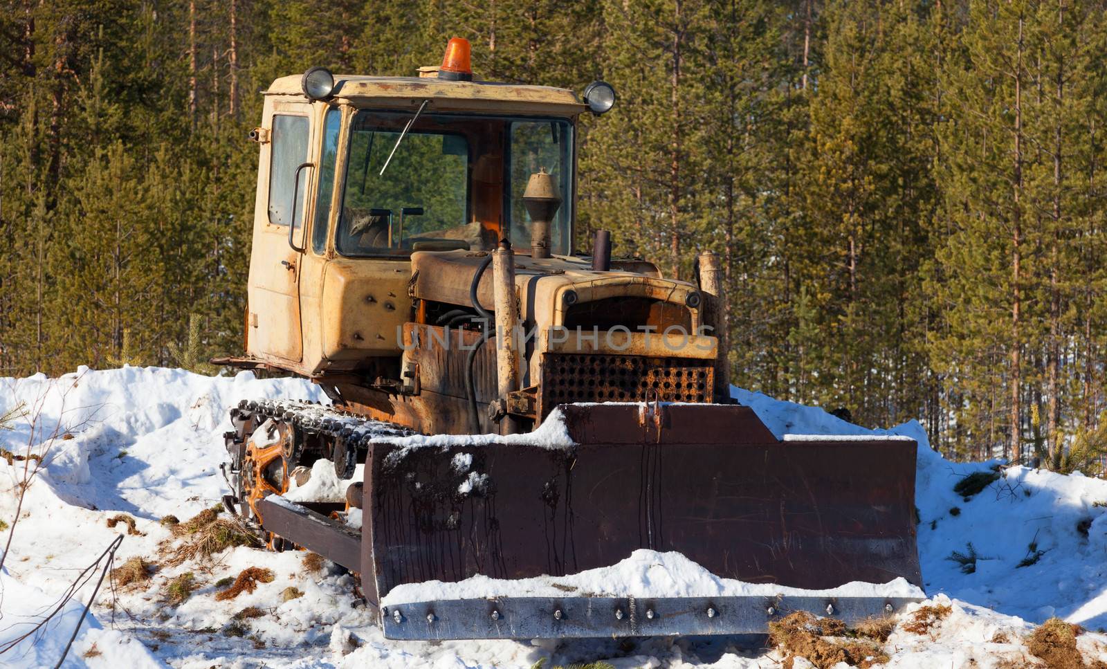 Old tractor-bulldozer cleans snow on the edge of the forest