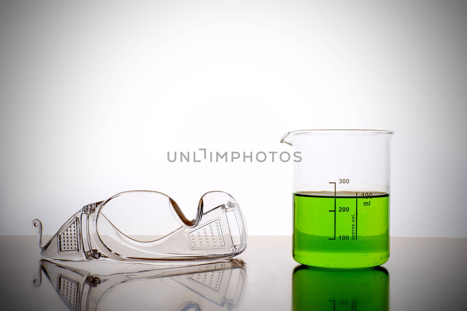 Measuring glass with green liquid and safety glasses, goggles in a chemical lab