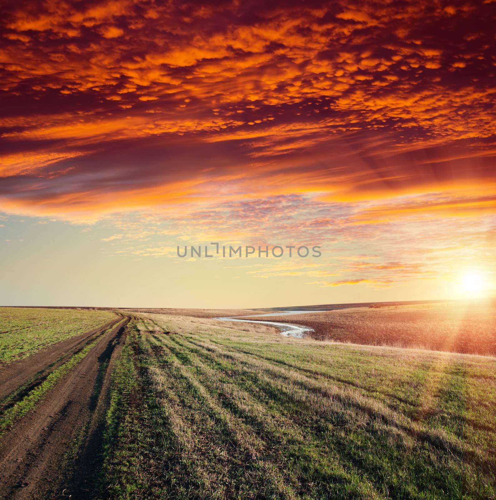 red sunset over river and rural road with dramatic sky by mycola