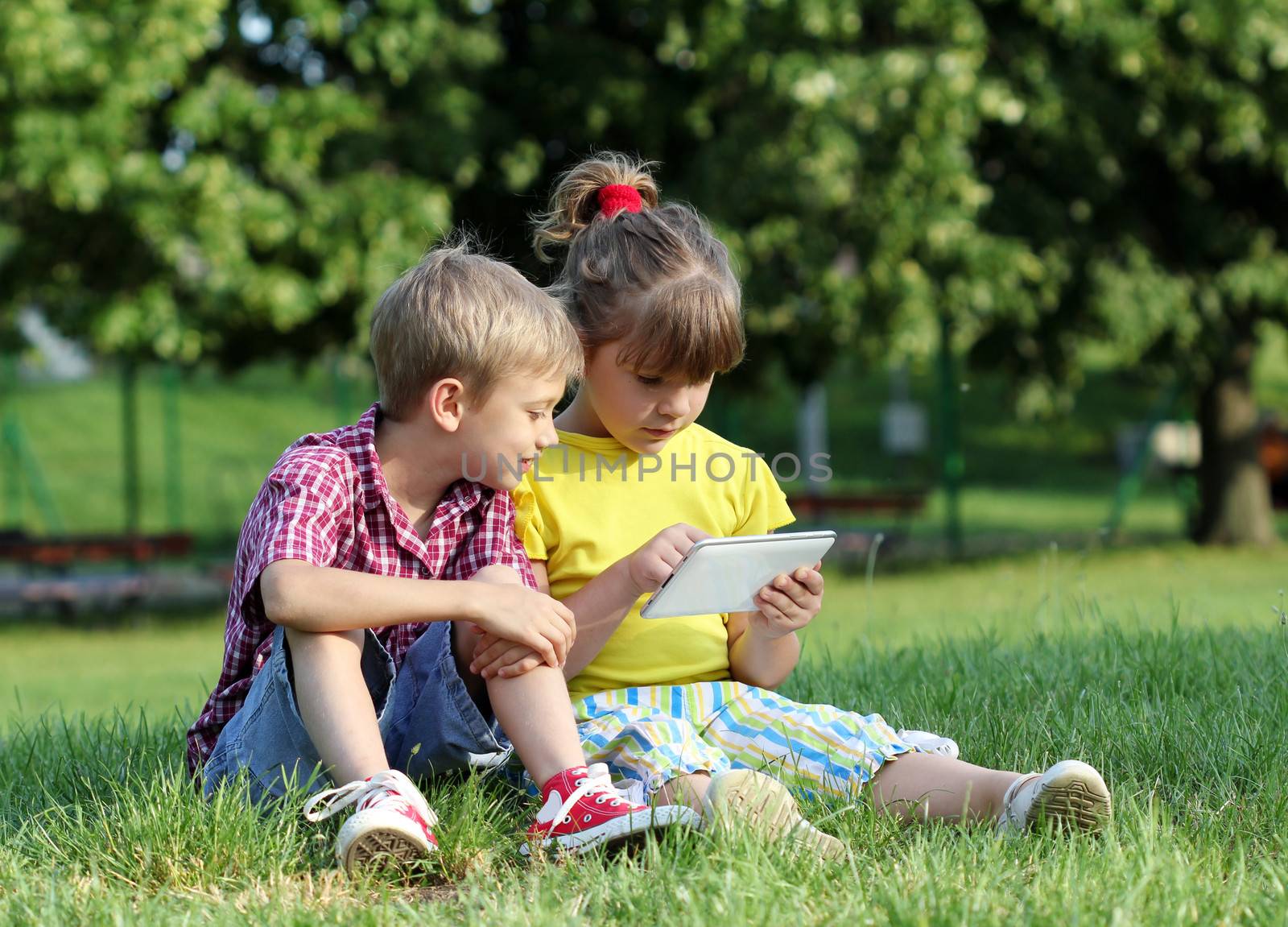 little girl and boy with tablet in park by goce