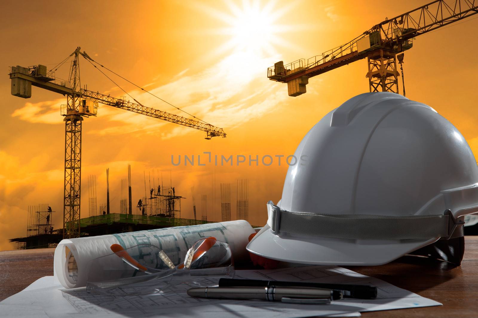 safety helmet and architect pland on wood table with sunset scen by khunaspix
