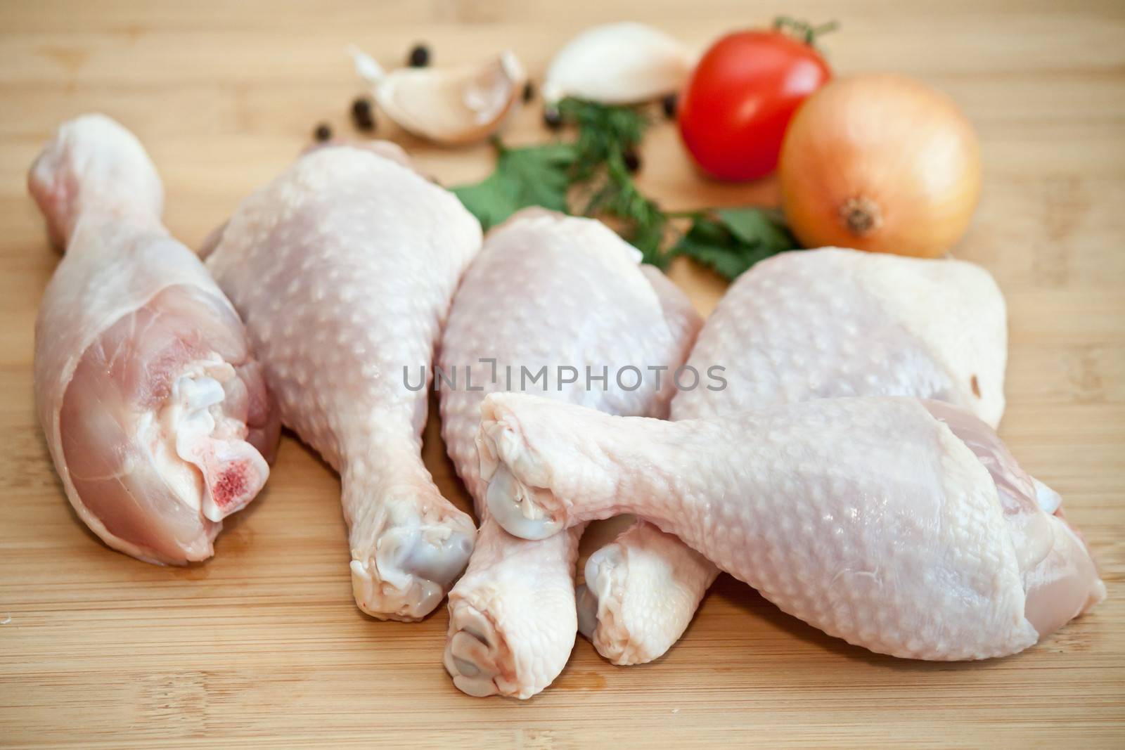 Raw chicken legs with vegetables and spices on the chopping board
