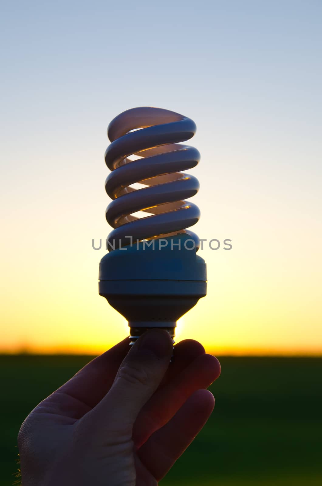 energy saving lamp in hand over sunset