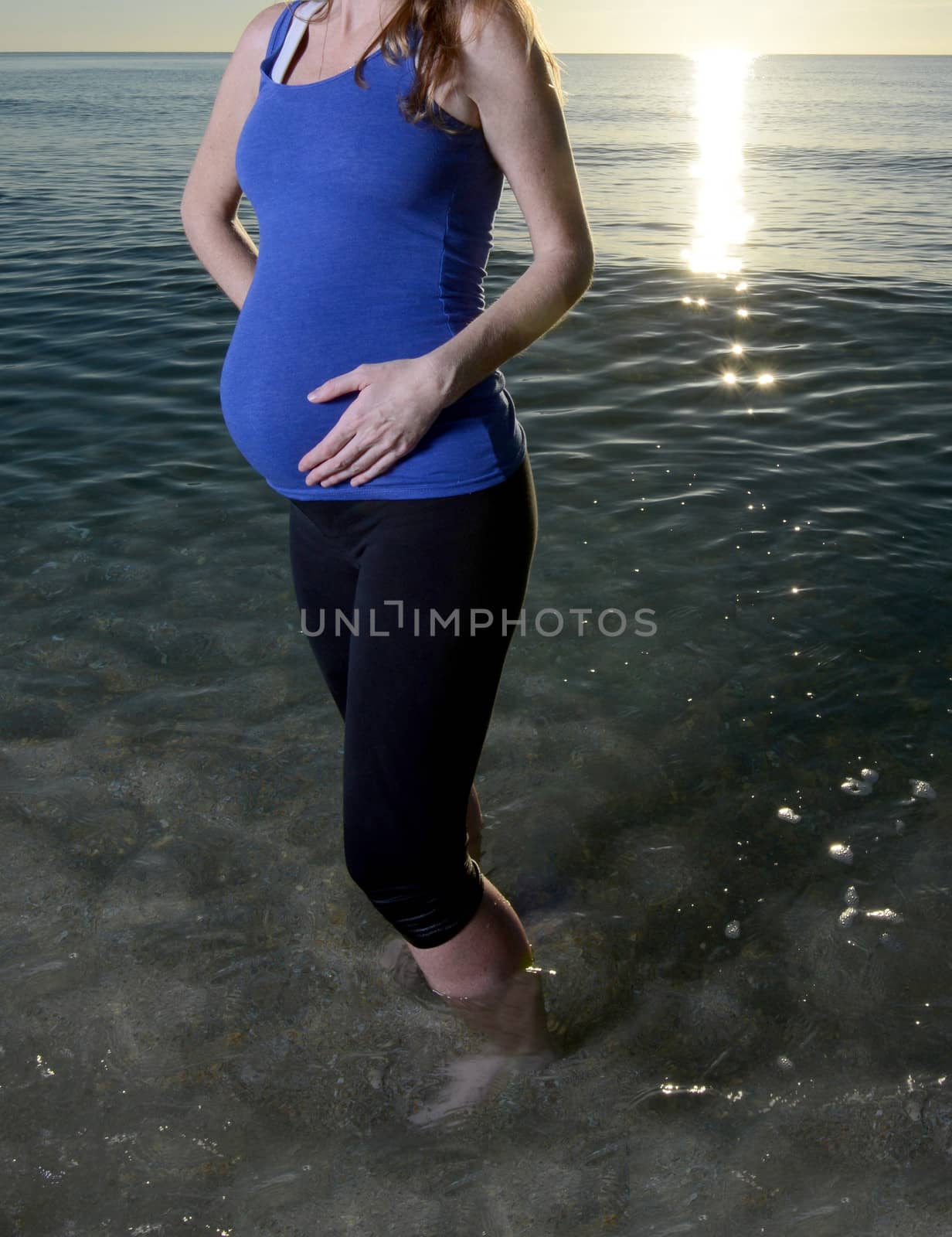 pregnant woman holding stomach standing in ocean at beach
