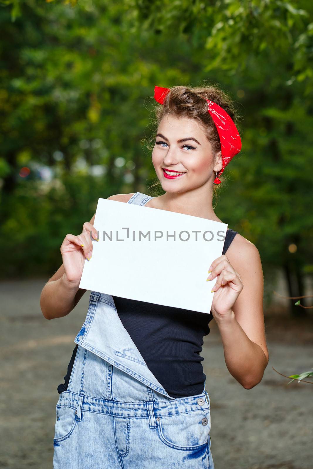 Beautiful pin-up girl in denim overalls and a red bandana holding copyspace