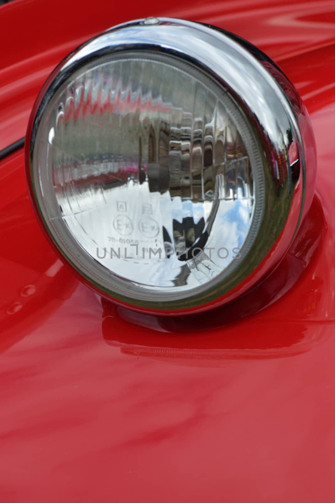 Detail of car headlamp on red in portrait