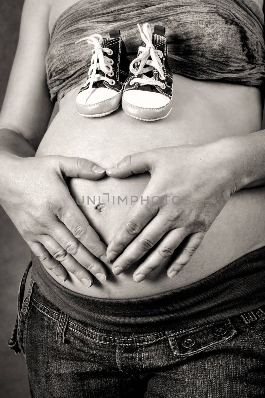 pregnant woman with a child's shoe tenderly holding her tummy with hand as heart shape