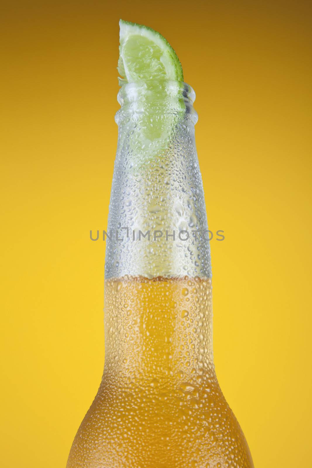 Mexican beer with a lime slice over a yellow background.