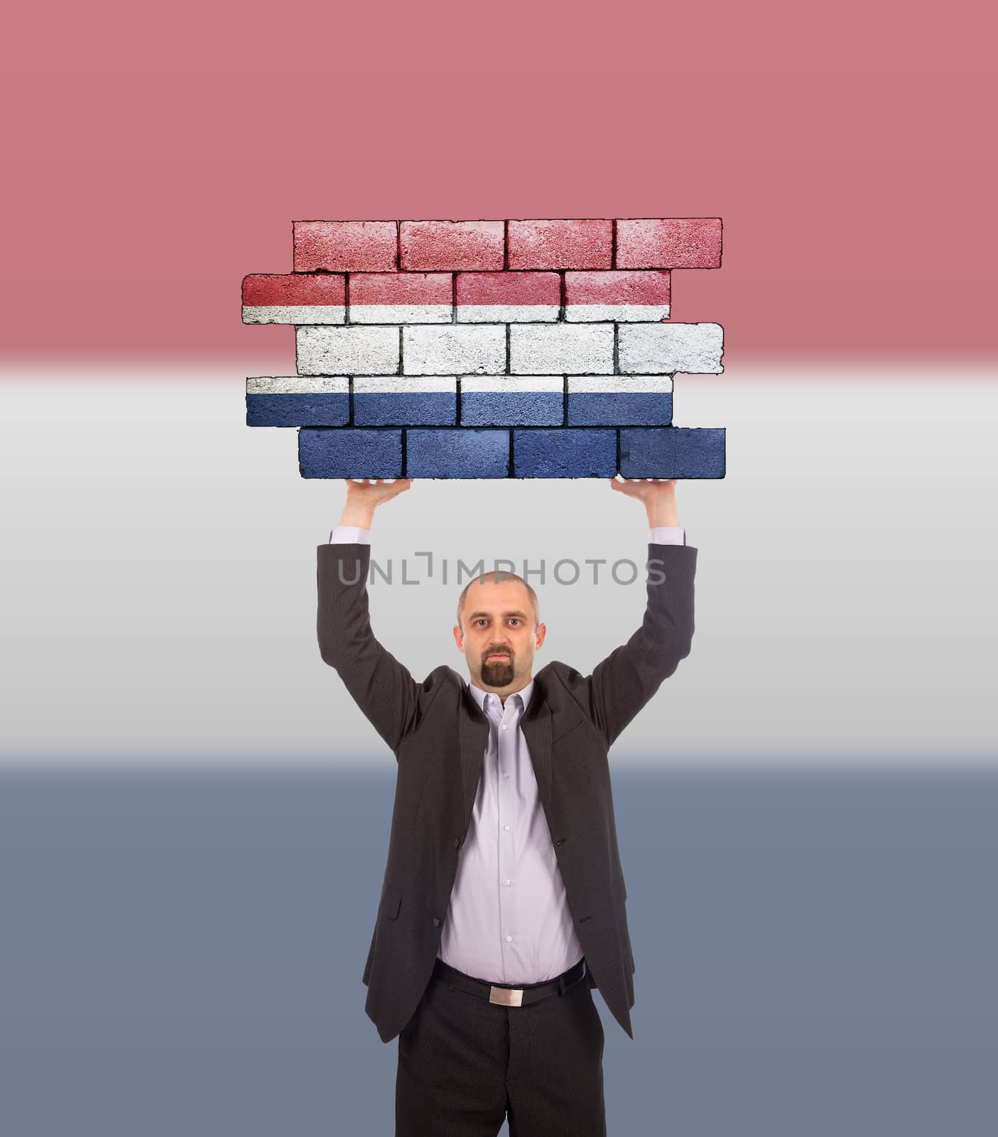 Businessman holding a large piece of a brick wall, flag of Netherlands, isolated on national flag