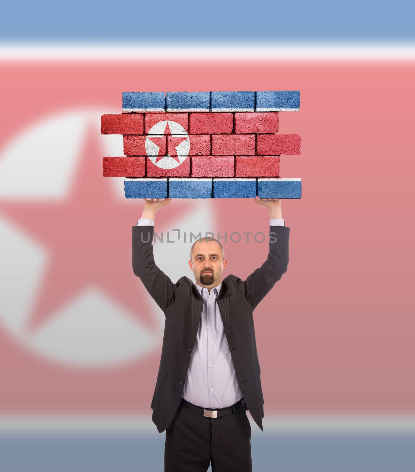 Businessman holding a large piece of a brick wall, flag of North Korea, isolated on national flag