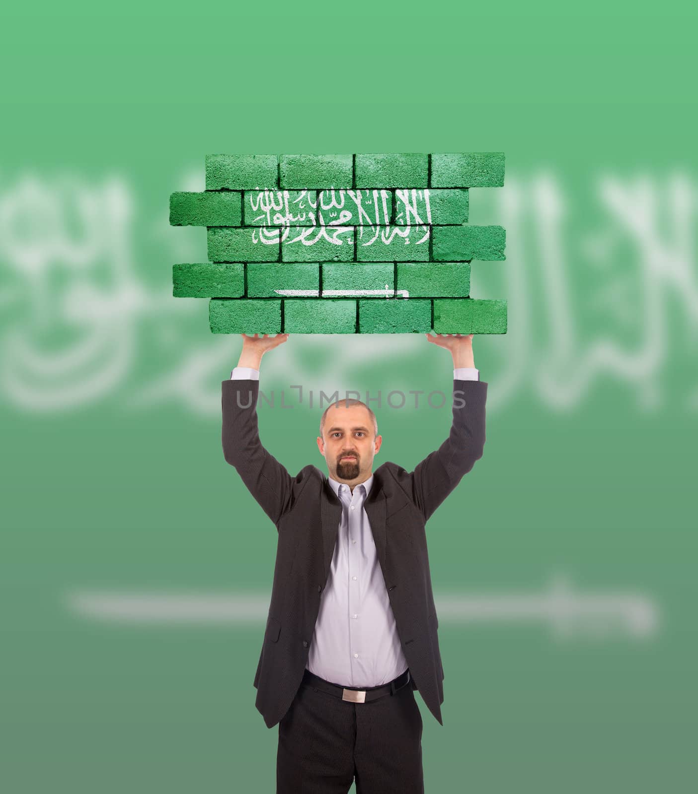 Businessman holding a large piece of a brick wall, flag of Saudi Arabia, isolated on national flag
