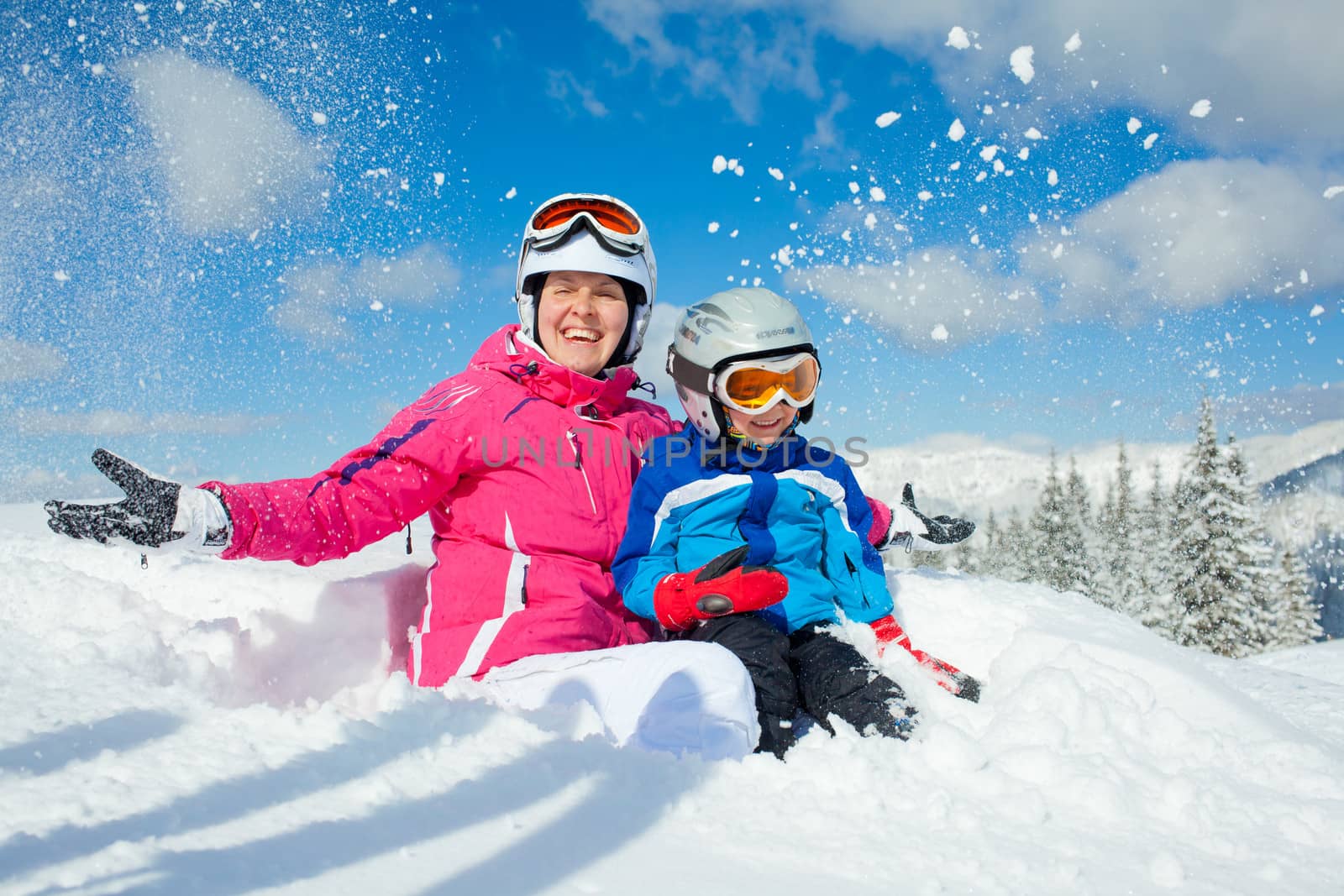 Skiing, winter, family - smiling boy in ski goggles and a helmet with his mother playing in snow in winter resort