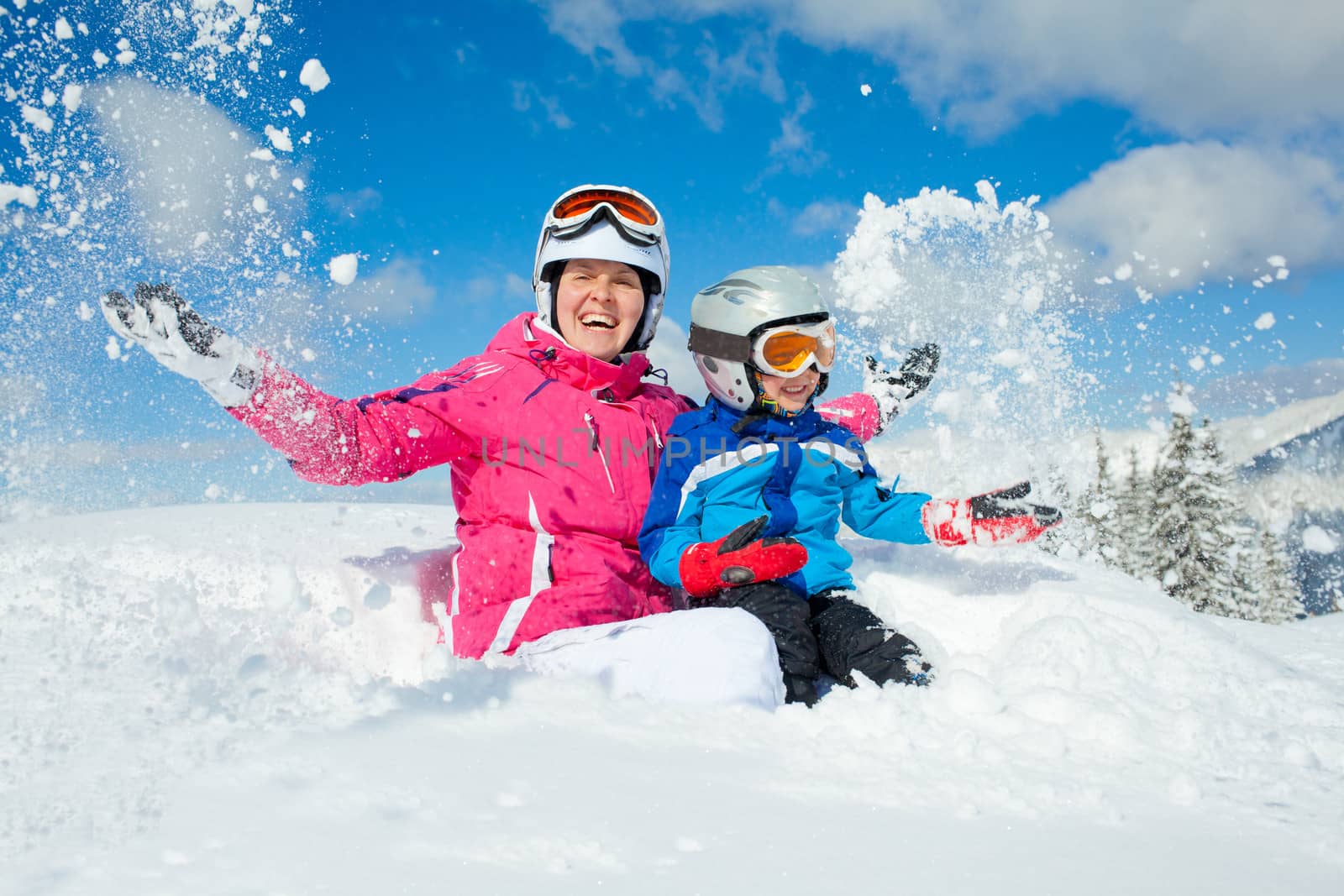 Skiing, winter, family - smiling boy in ski goggles and a helmet with his mother playing in snow in winter resort