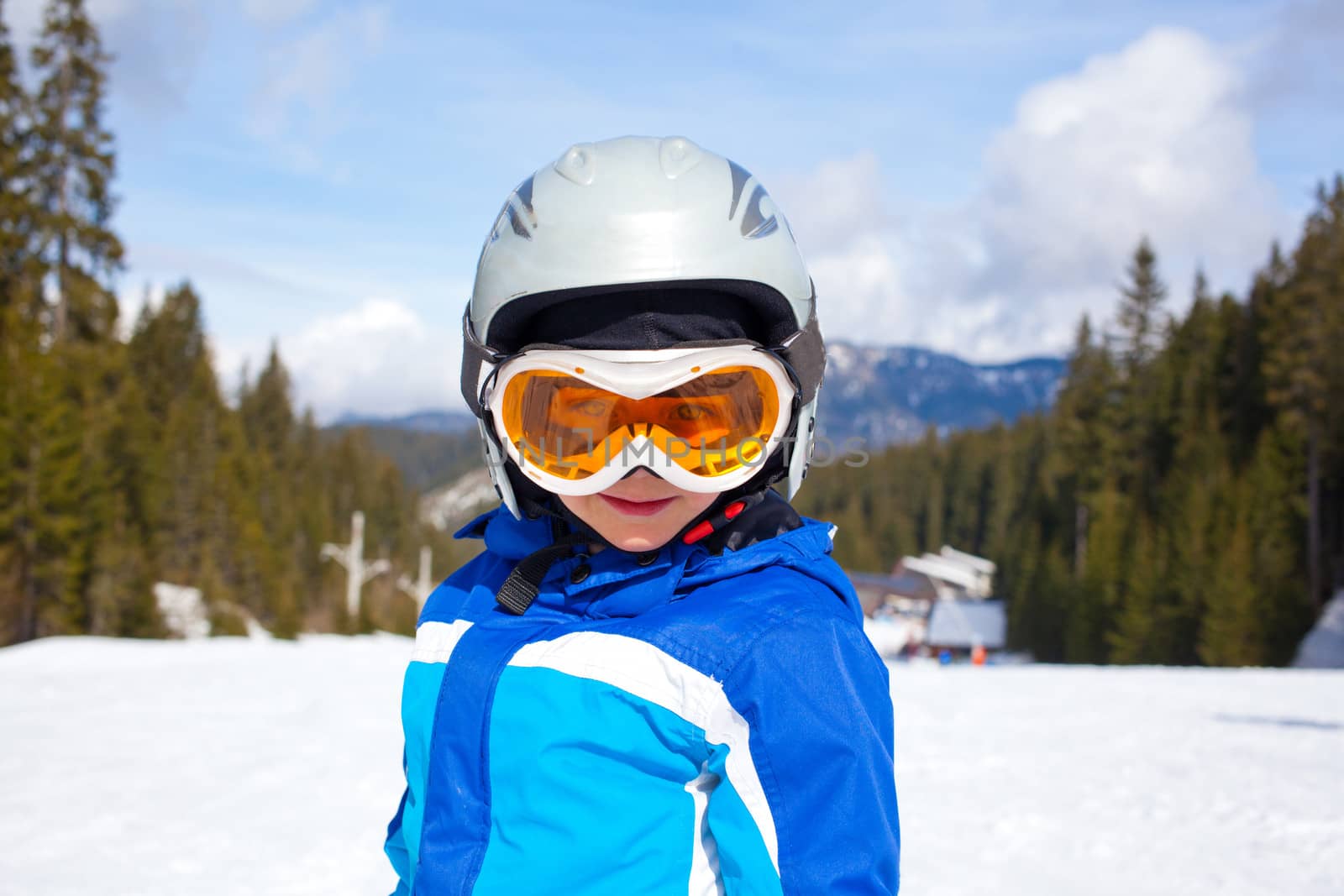 Portrait of little boy in helmet and ski goggles on a sunny day in the mountains. Active outdoor childhood concept