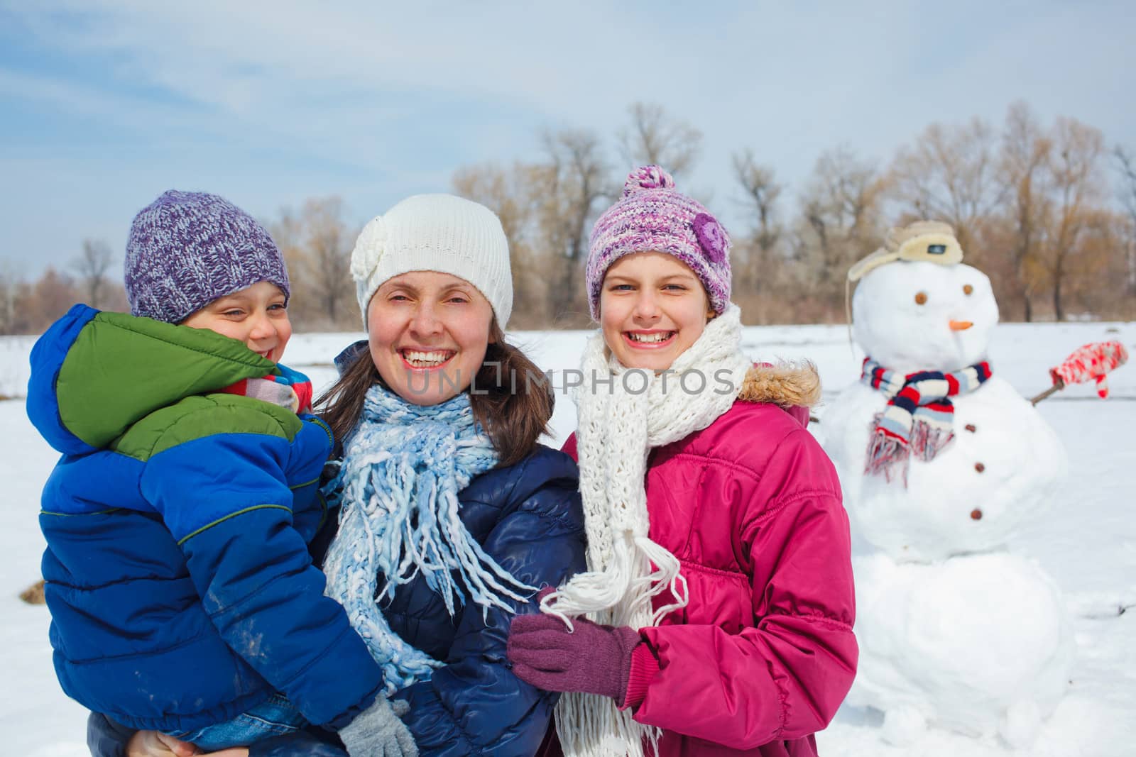 Happy mother with two kids building snowman outside in winter time