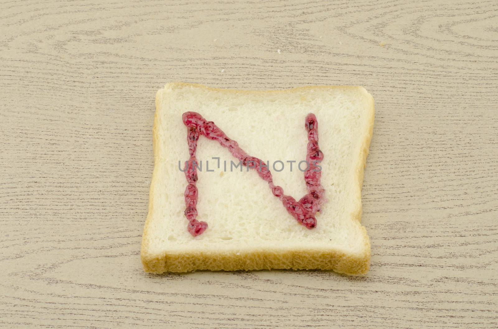 jam alphabet on sliced bread on wood background