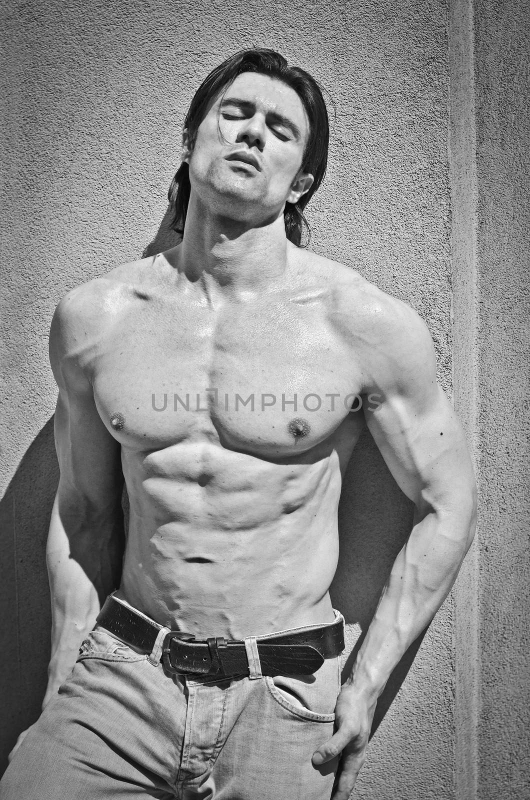 Attractive young man shirtless with jeans leaning against a wall with his eyes closed, black and white shot
