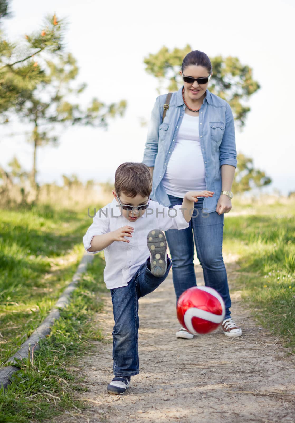 Happy son playing with soccer ball, and his pregnacy mother look by doble.d