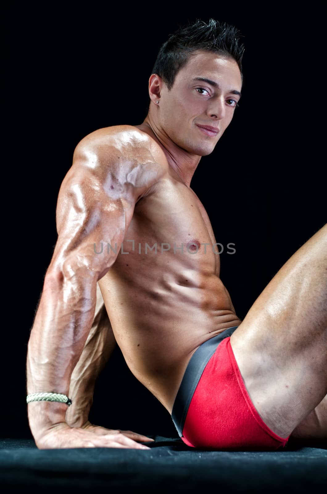 Handsome young man with muscular body, sitting on the floor showing ripped tricep, arm and abs