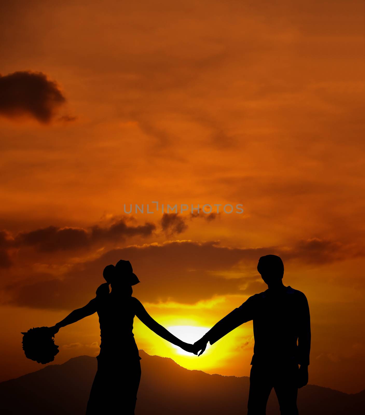 Silhouette of loving couple standing on a hill against the sun and mountains range