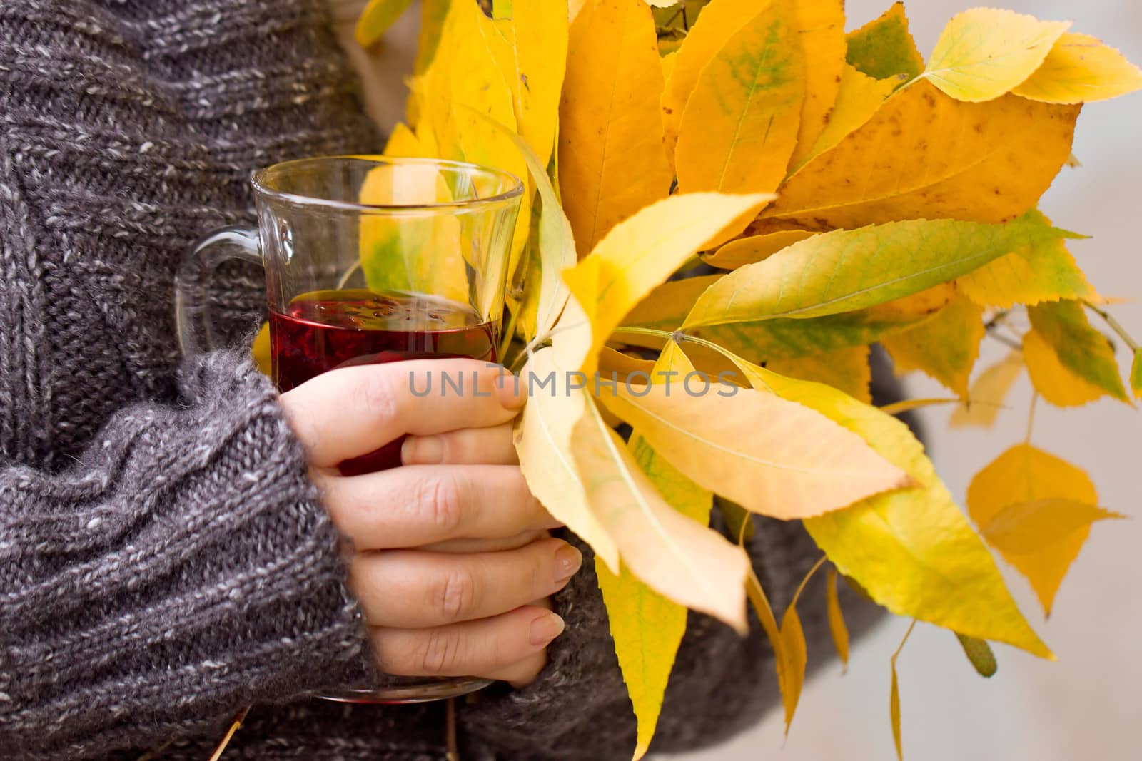 Female hand holding a glass of tea and autumn leaves