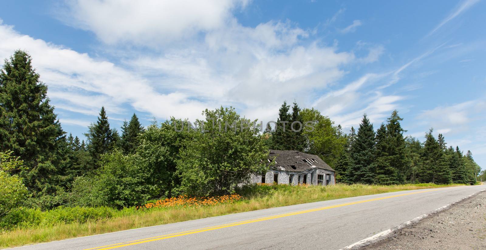 An old abandoned building is sitting along the highway surrounded by the beauty of the Maine countryside.