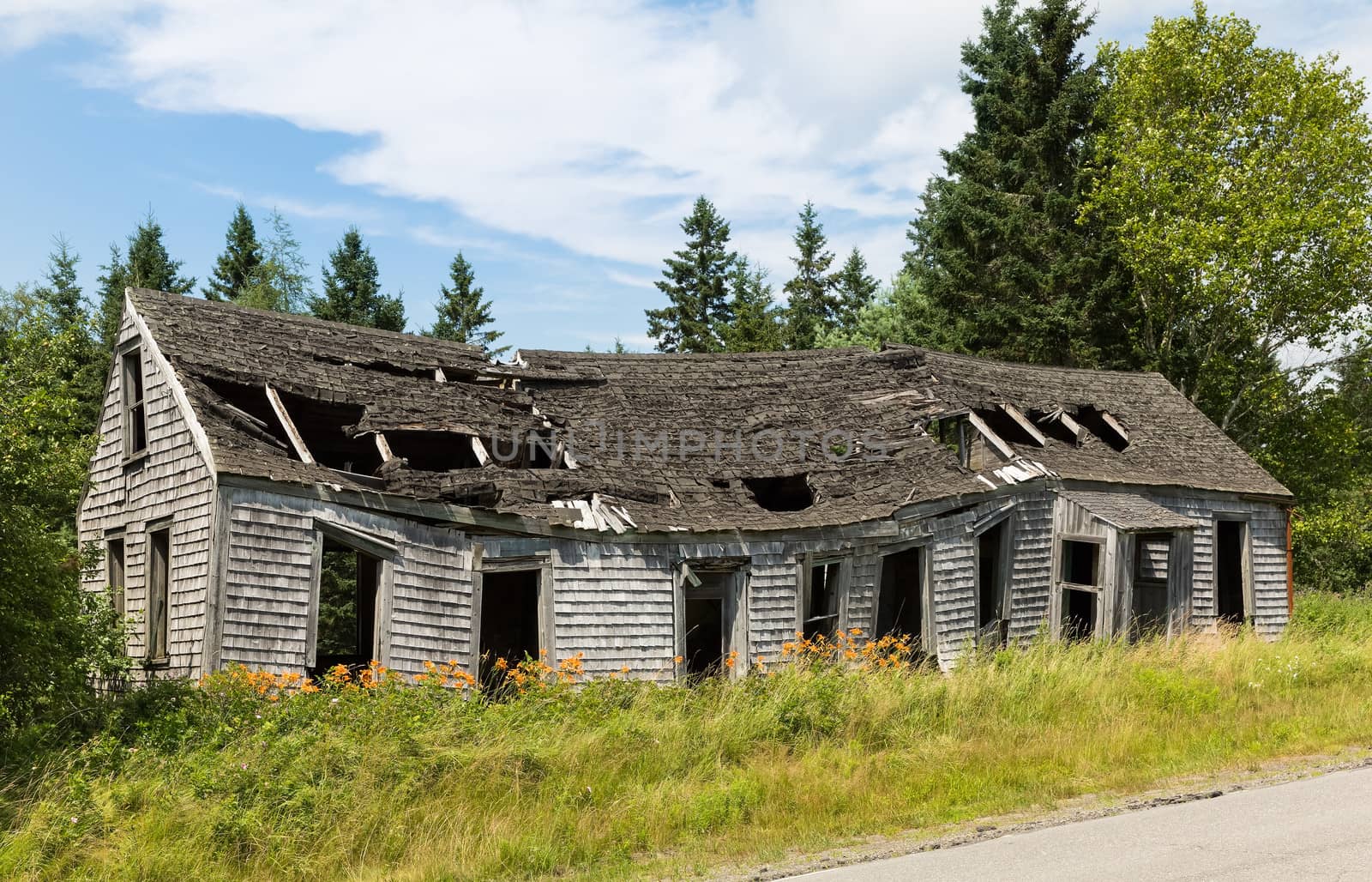 An old abandoned building is sitting along the highway surrounded by the beauty of the Maine countryside.