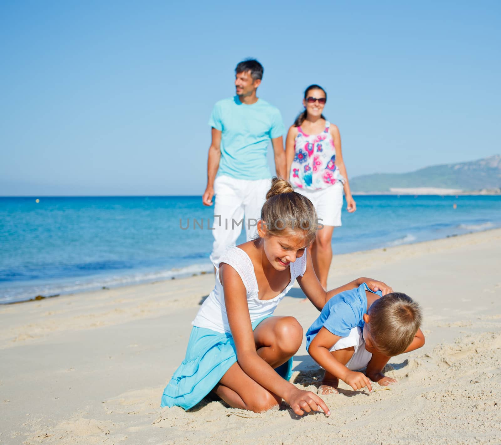 Two cute kids playing on tropical beach with their parents