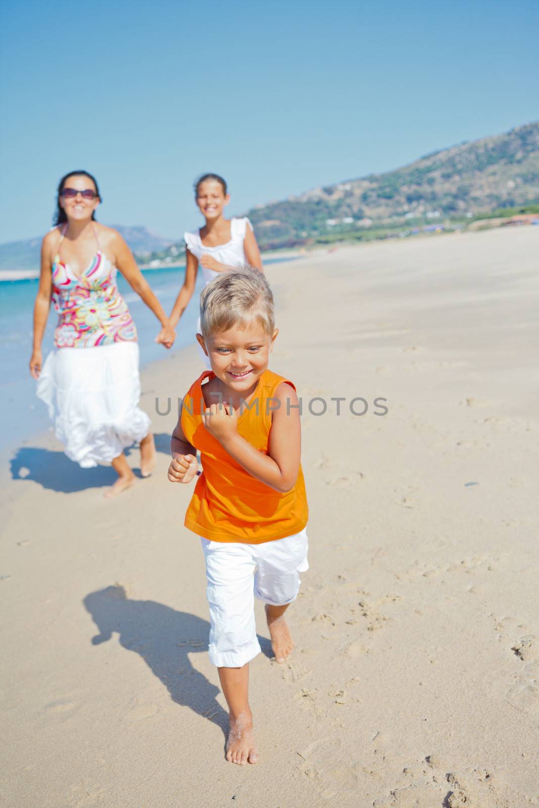 Adorable happy boy with sister and mother running on beach