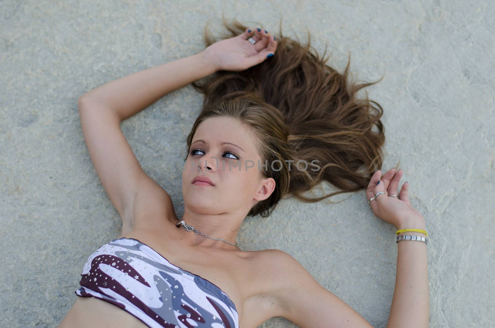 Pretty brunette girl in bikini lying on stone with hair pulled up