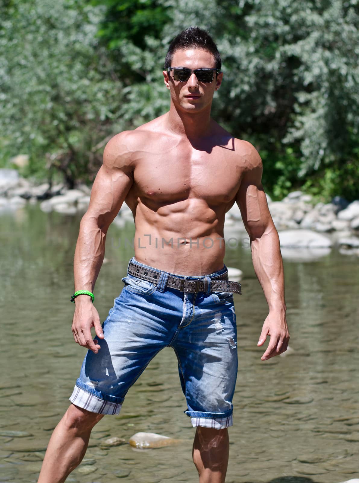 Handsome young muscle man standing in water pond, naked wearing only jeans