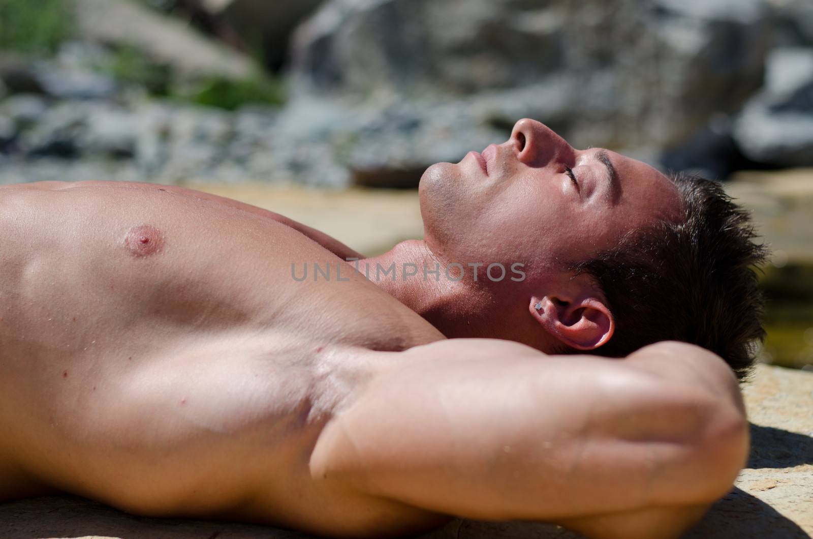 Attractive young man  laying naked on white rocks, eyes closed, side or profile view