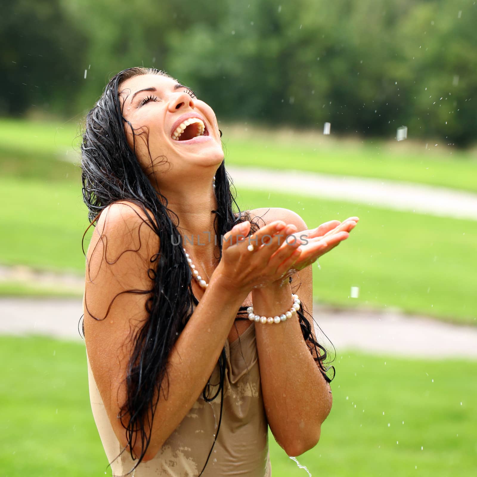 Young sexy brunette woman outdoor in a garden playing with water and rain with wet shirt