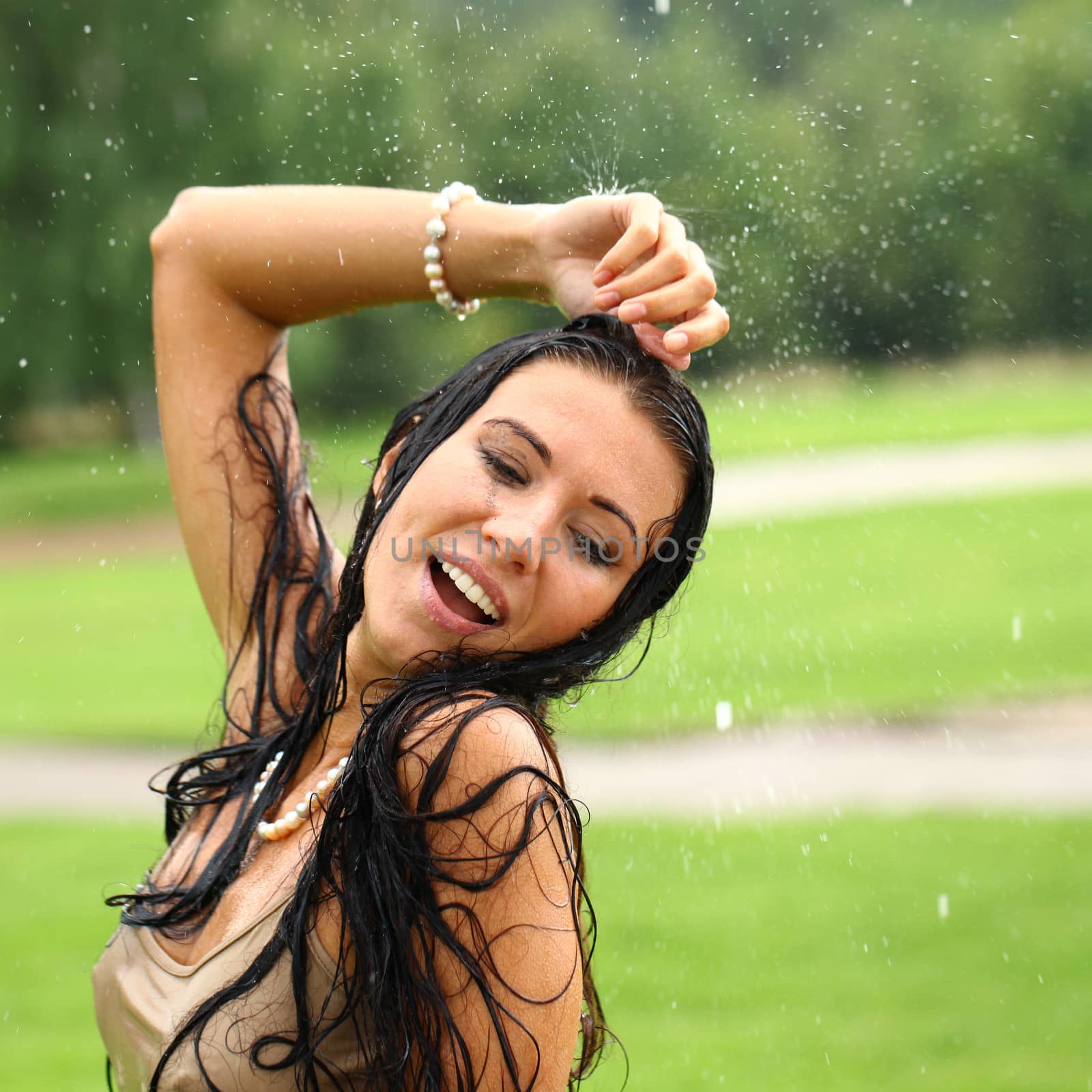 Young sexy brunette woman outdoor in a garden playing with water and rain with wet shirt