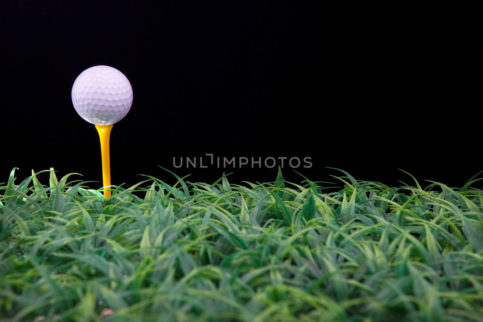 golf ball on yellow tee with green grass isolated black