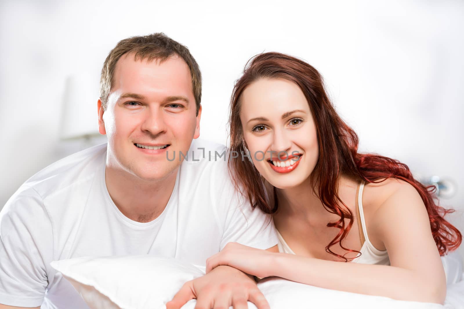 Young man and woman lying together in bed, smiling and happy