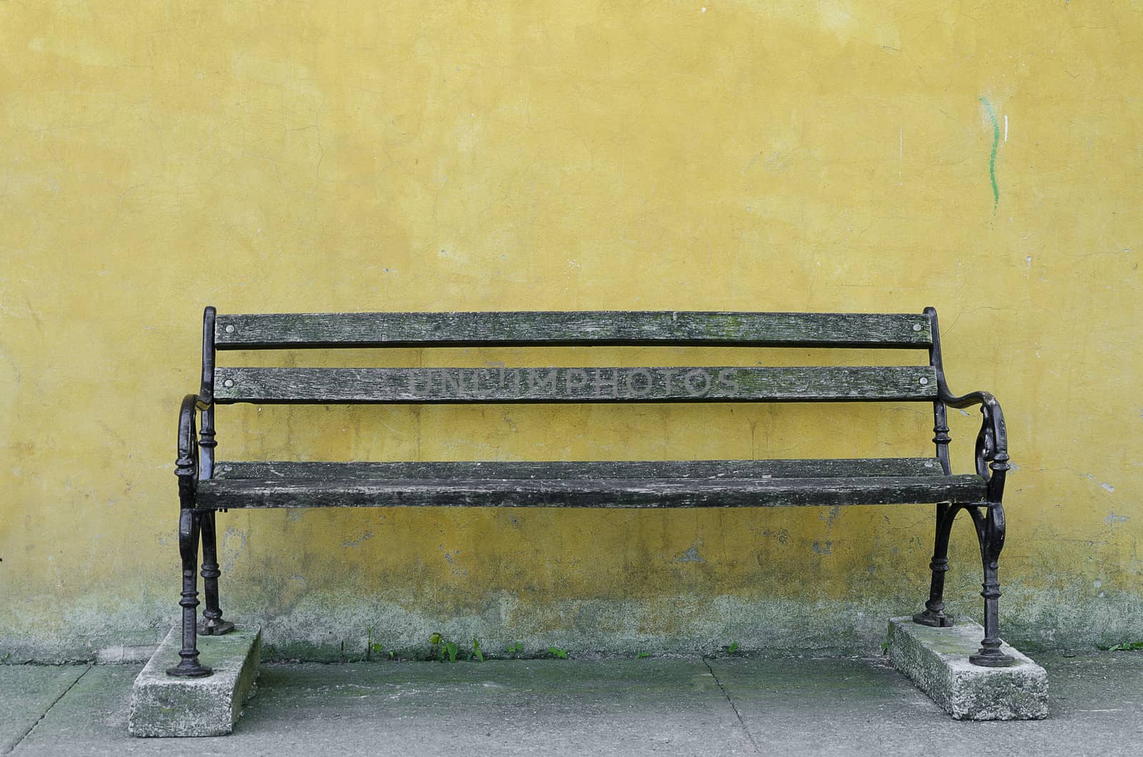 old park bench in front of a yellow wall