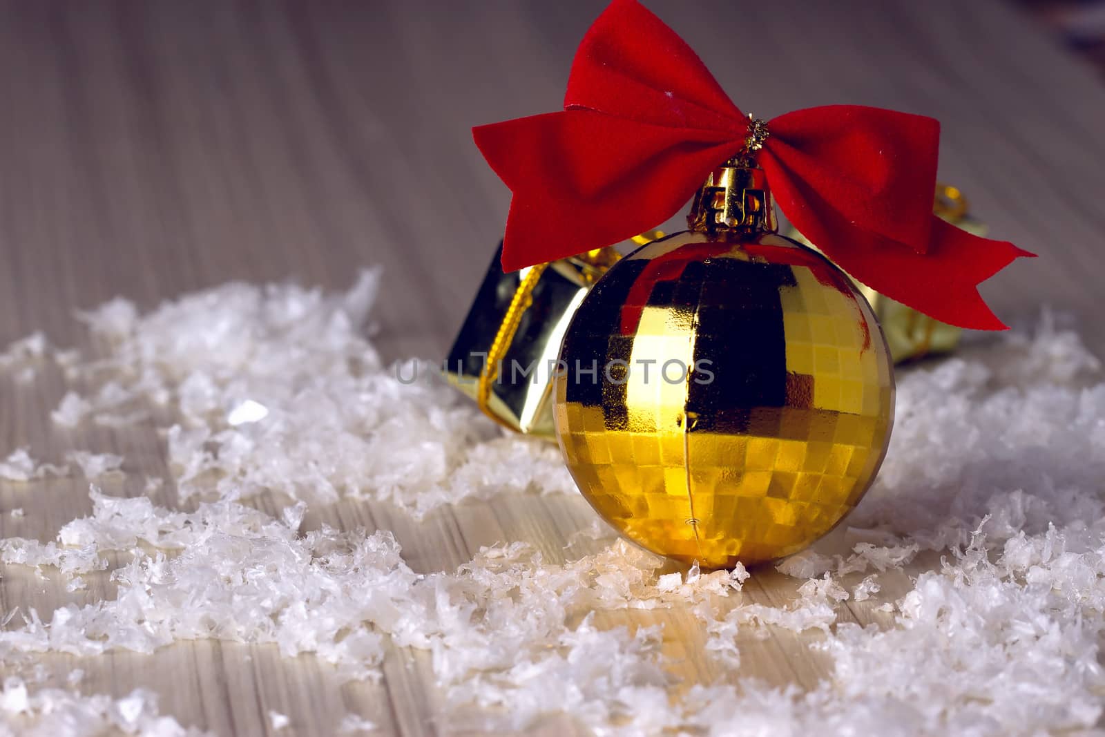 Golden ball with a red bow lying in the snow and beads