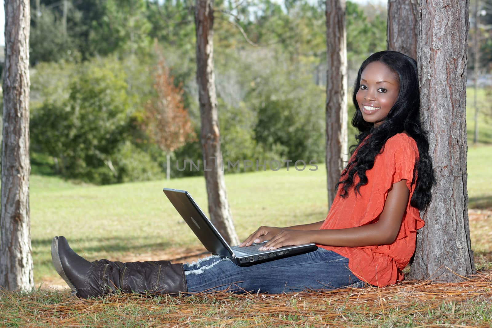 An extraordinarily beautiful young woman with a captivating smile, dressed in casual wear, works on her laptop computer outdoors.