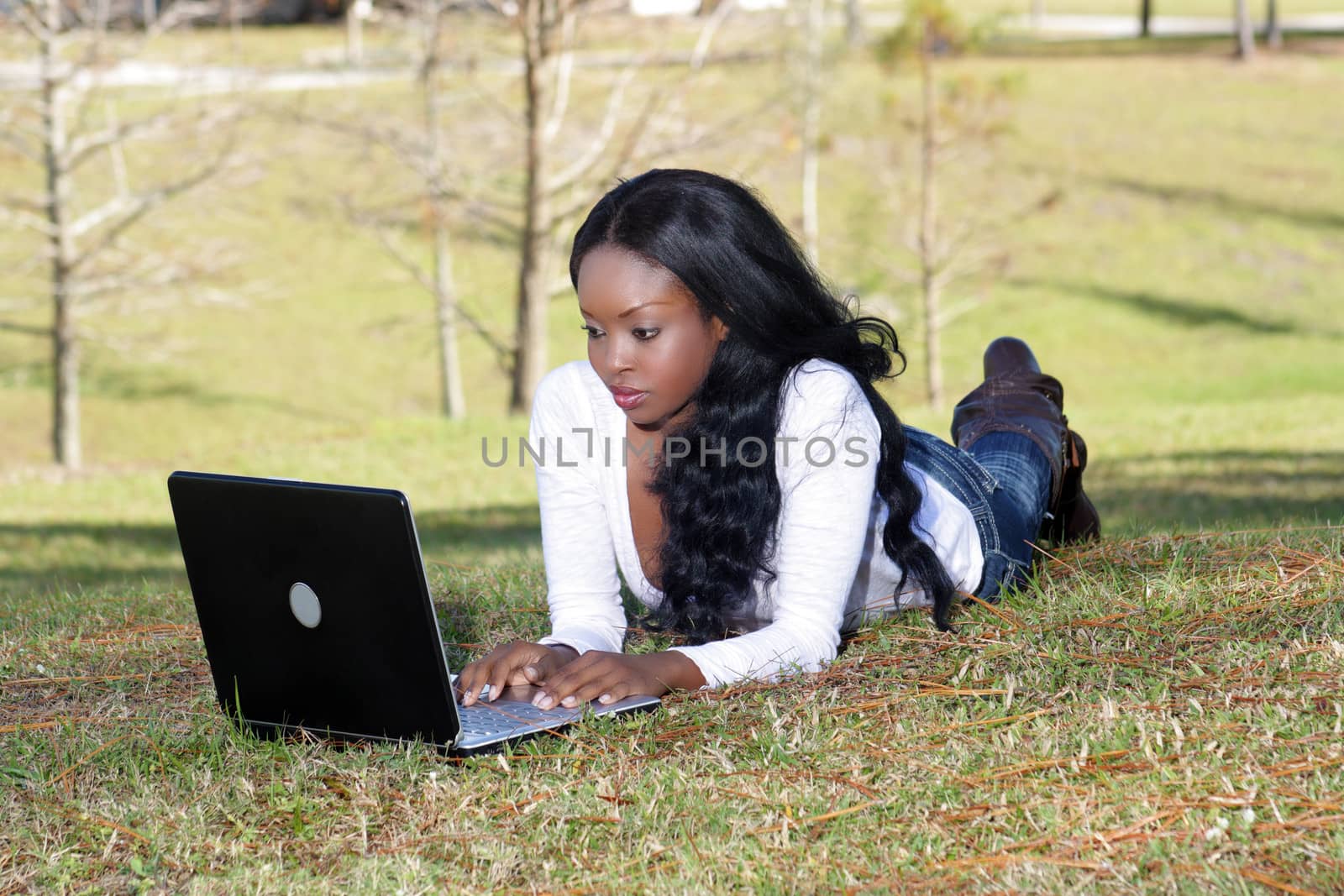 An extraordinarily beautiful young woman dressed in casual wear, works on her laptop computer outdoors.