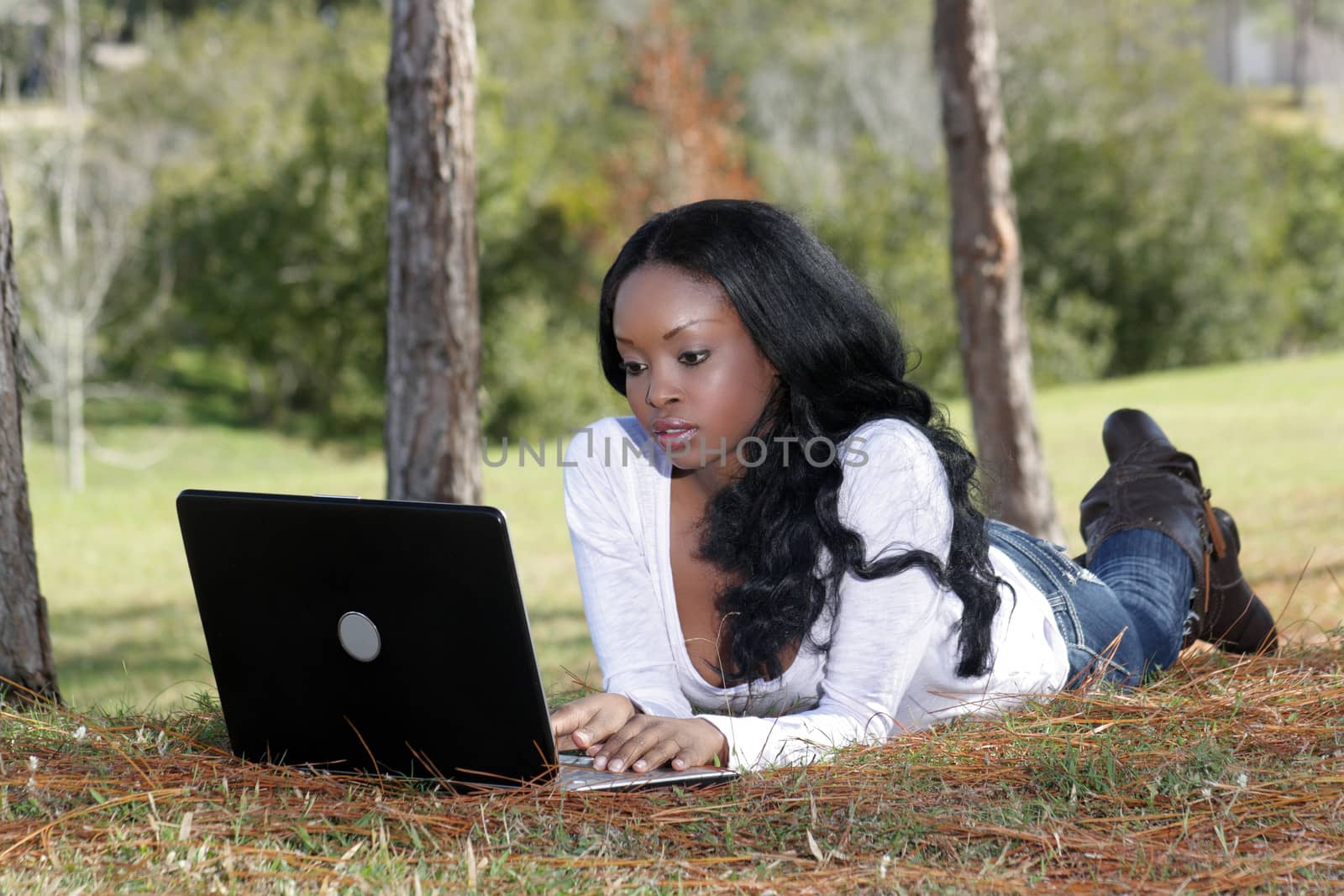 An extraordinarily beautiful young woman dressed in casual wear, works on her laptop computer outdoors.