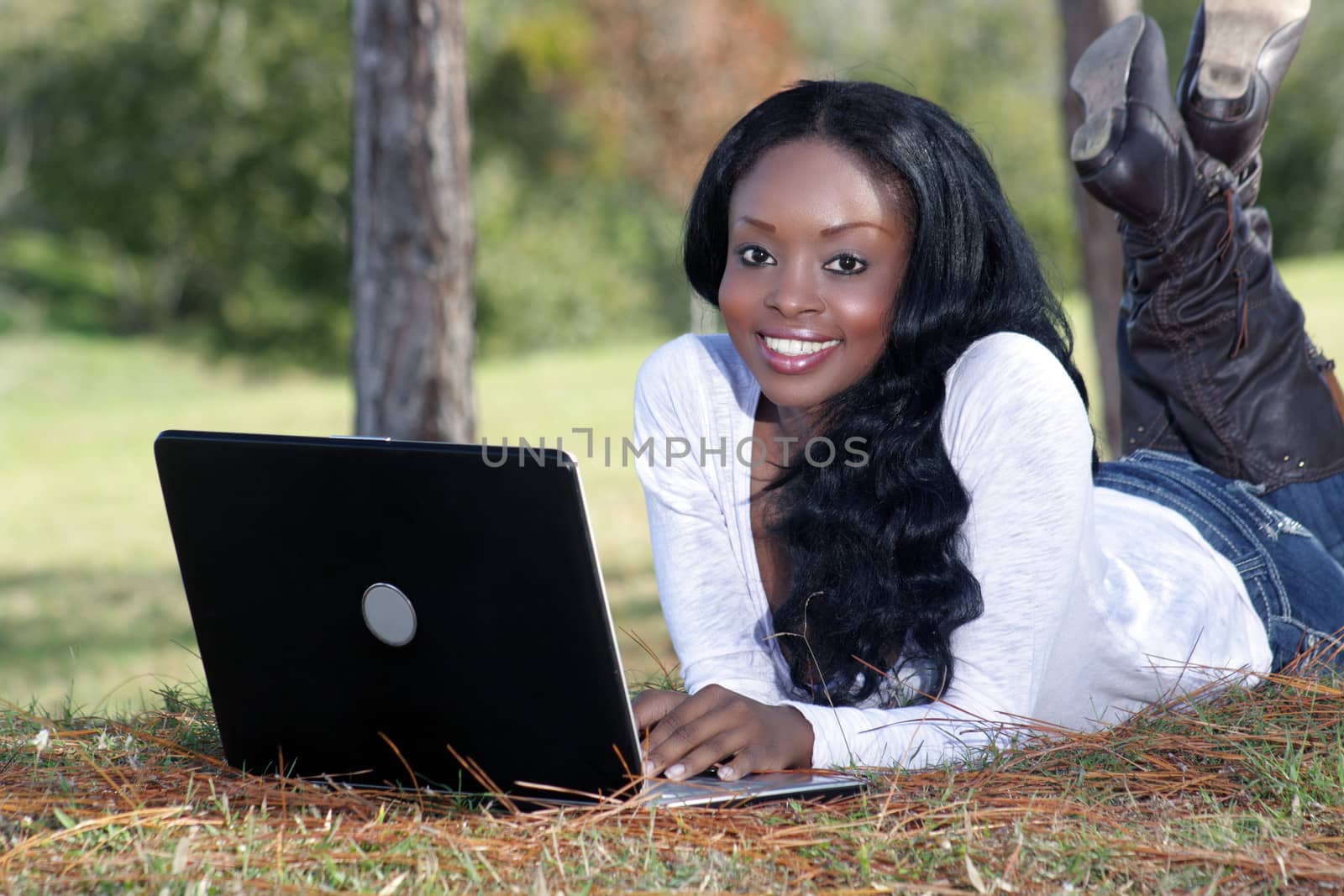 An extraordinarily beautiful young woman with a captivating smile, dressed in casual wear, works on her laptop computer outdoors.